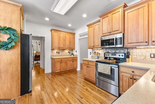 kitchen with light countertops, light wood finished floors, crown molding, and appliances with stainless steel finishes