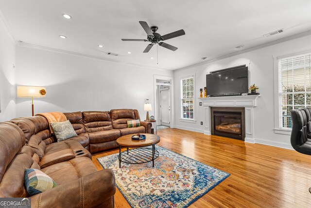 living area featuring visible vents, crown molding, a glass covered fireplace, and wood finished floors