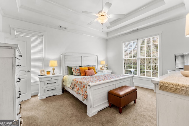 bedroom with a tray ceiling, light colored carpet, visible vents, and ornamental molding