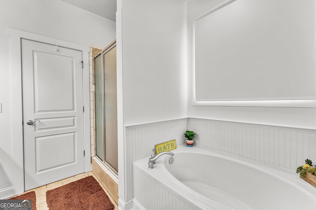 full bath with a stall shower, a wainscoted wall, a bath, and tile patterned flooring