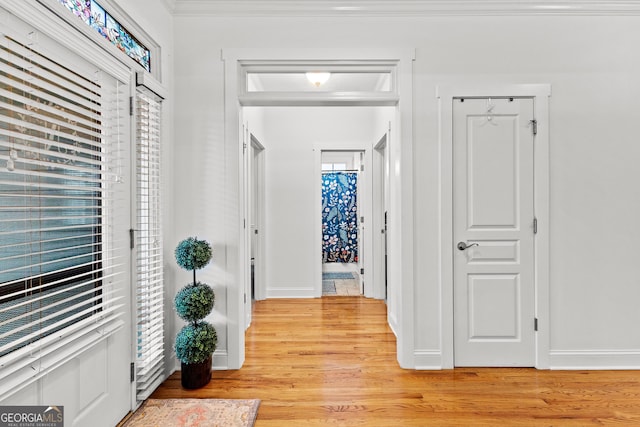 hallway featuring crown molding, baseboards, and light wood finished floors