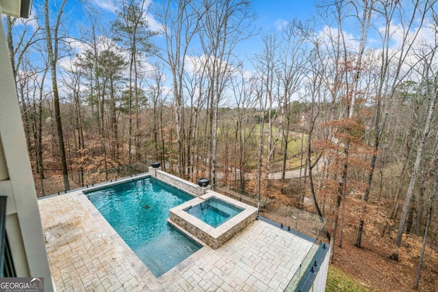 view of swimming pool with a patio, a forest view, and a pool with connected hot tub