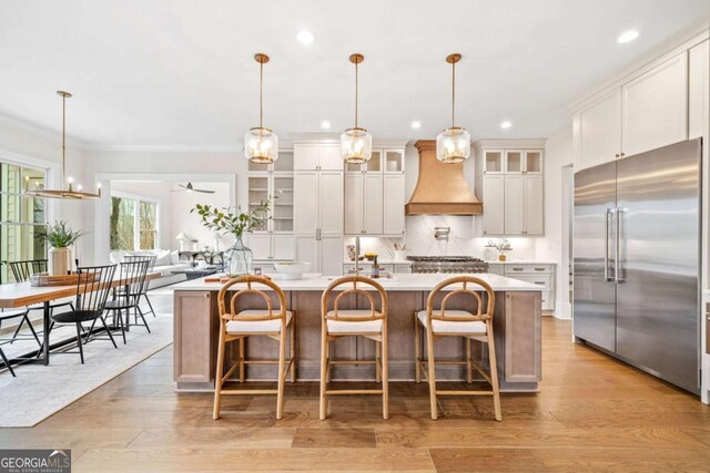 kitchen with a center island with sink, tasteful backsplash, light countertops, custom range hood, and built in refrigerator