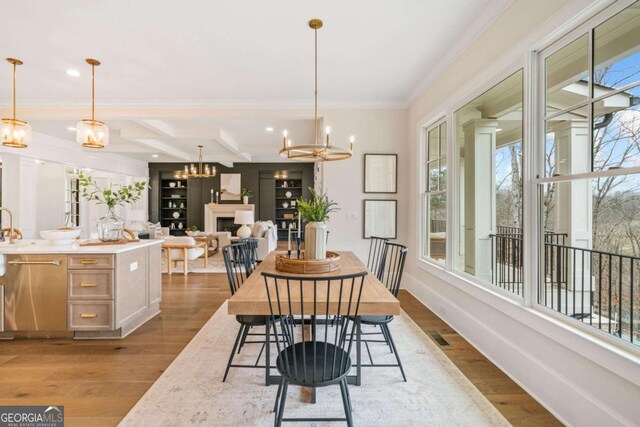 dining room featuring crown molding, a notable chandelier, a fireplace, wood finished floors, and baseboards