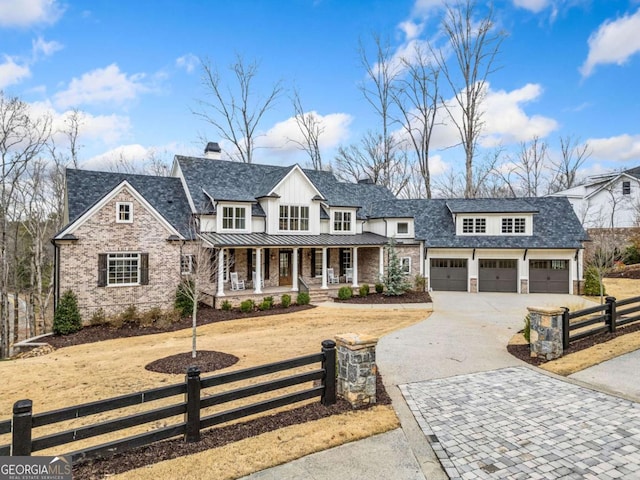 modern farmhouse featuring a porch, a fenced front yard, an attached garage, driveway, and a standing seam roof