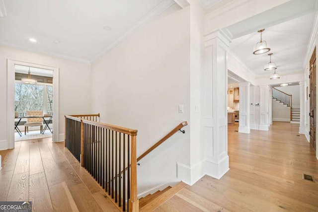 hall with visible vents, ornamental molding, light wood-style flooring, and an upstairs landing