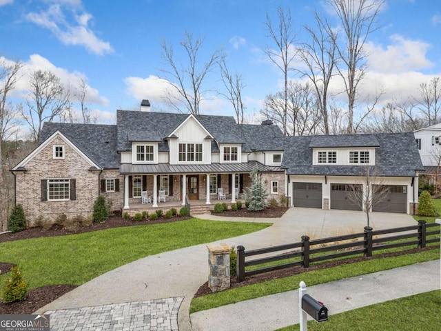 modern farmhouse featuring a fenced front yard, a chimney, an attached garage, a standing seam roof, and a porch