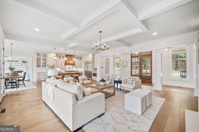 living area with a chandelier, beam ceiling, visible vents, and light wood-style flooring