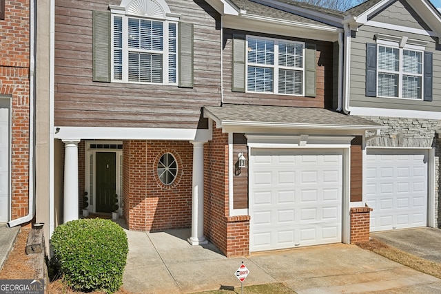 townhome / multi-family property featuring a garage, concrete driveway, brick siding, and roof with shingles