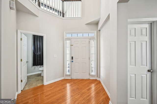 foyer entrance with baseboards, a towering ceiling, and light wood finished floors