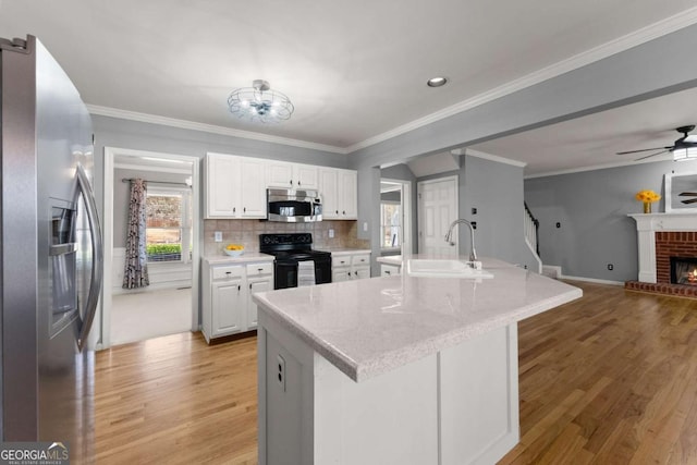 kitchen featuring a sink, white cabinetry, open floor plan, appliances with stainless steel finishes, and a brick fireplace