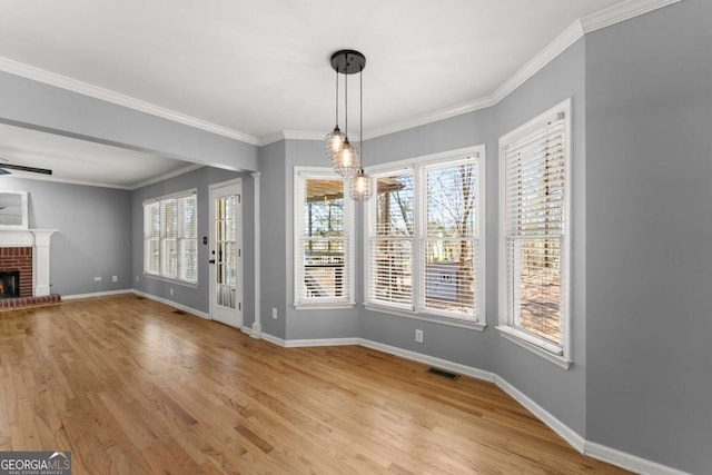 unfurnished dining area with visible vents, baseboards, light wood-style flooring, ornamental molding, and a brick fireplace