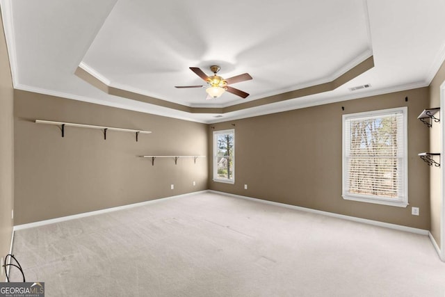 carpeted empty room featuring a tray ceiling, crown molding, visible vents, ceiling fan, and baseboards