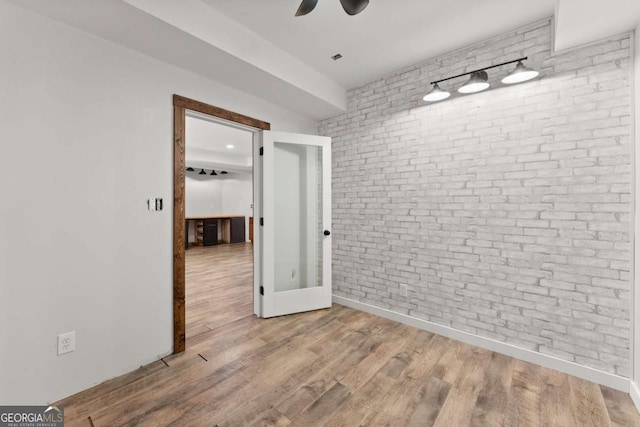 spare room with brick wall, baseboards, ceiling fan, and wood finished floors