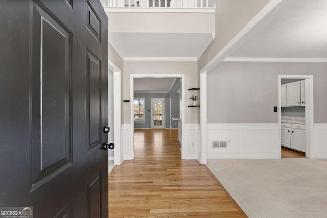 entryway with light wood-style floors, a wainscoted wall, visible vents, and crown molding