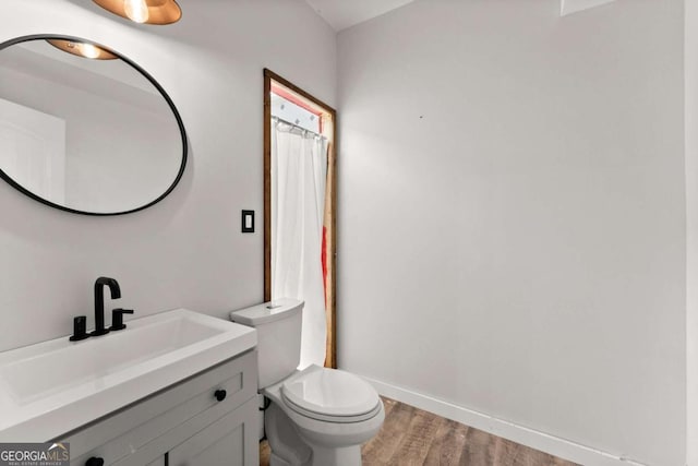 bathroom featuring baseboards, a shower with shower curtain, toilet, wood finished floors, and vanity