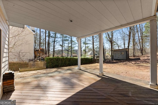 wooden terrace featuring an outbuilding, fence, and a storage unit