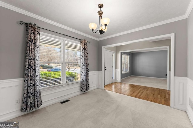 carpeted foyer entrance featuring ornamental molding, wainscoting, a notable chandelier, and visible vents