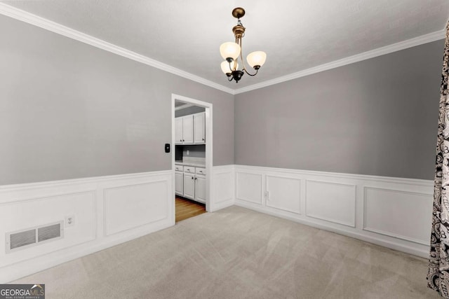 unfurnished room with crown molding, visible vents, an inviting chandelier, wainscoting, and light carpet