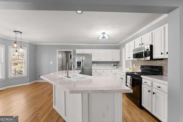 kitchen with an island with sink, appliances with stainless steel finishes, ornamental molding, light countertops, and light wood-style floors