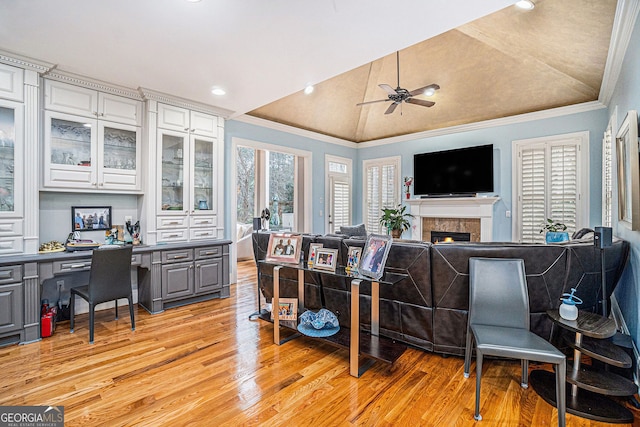 interior space with ceiling fan, lofted ceiling, ornamental molding, a warm lit fireplace, and light wood-style floors