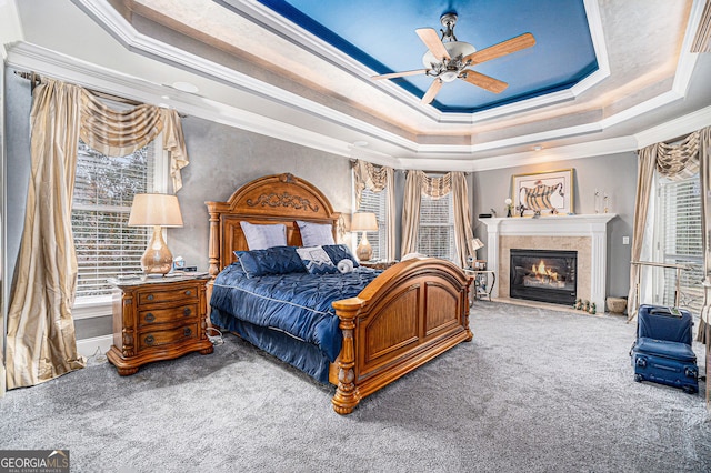 bedroom featuring a ceiling fan, a tray ceiling, a glass covered fireplace, crown molding, and carpet flooring