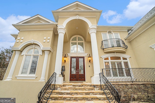 property entrance with a balcony, french doors, stone siding, and stucco siding