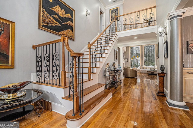 foyer entrance with stairway, ornamental molding, a towering ceiling, wood finished floors, and ornate columns