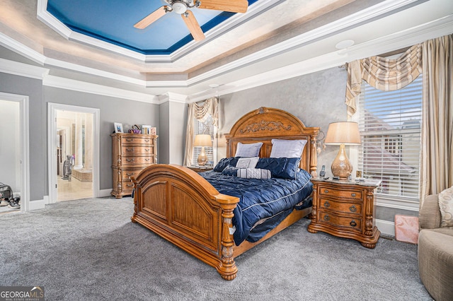 bedroom featuring ornamental molding, a tray ceiling, ensuite bath, carpet flooring, and ceiling fan