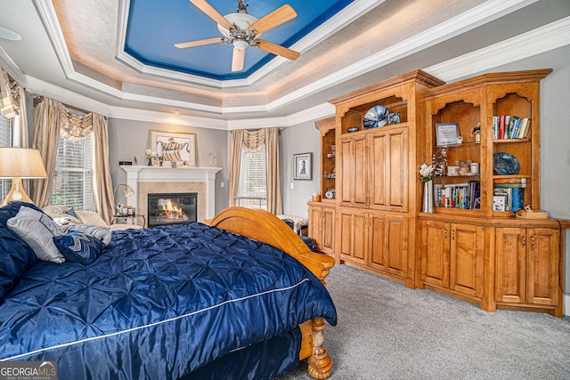 bedroom with a glass covered fireplace, a tray ceiling, carpet flooring, and crown molding