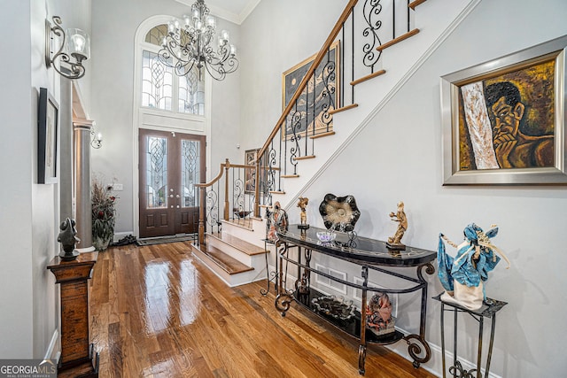 foyer entrance featuring stairs, ornamental molding, a high ceiling, an inviting chandelier, and wood finished floors