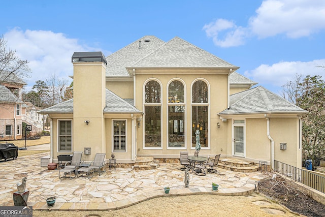 rear view of house featuring stucco siding, a patio, fence, a shingled roof, and a chimney