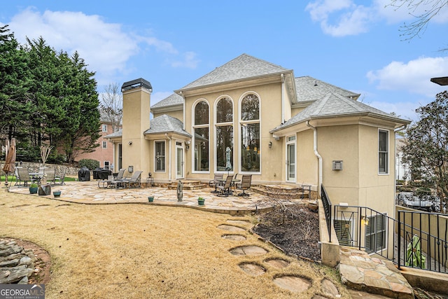 back of property with a patio area, stucco siding, a chimney, and a shingled roof