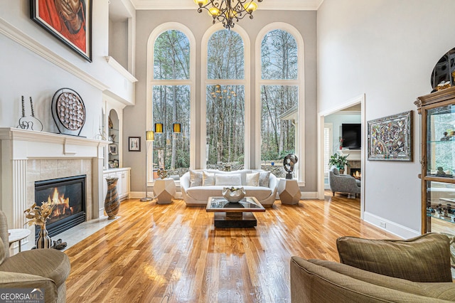 living area with a tiled fireplace, crown molding, baseboards, and wood-type flooring