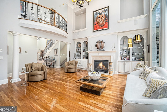 living area featuring stairway, decorative columns, wood finished floors, and baseboards