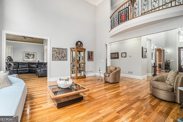 living room with wood finished floors, visible vents, a towering ceiling, and ornamental molding