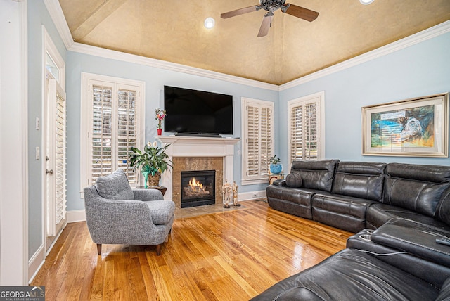 living room with a ceiling fan, wood finished floors, a high end fireplace, vaulted ceiling, and crown molding