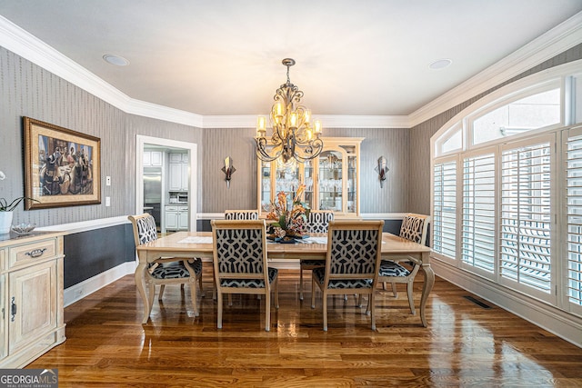 dining area featuring visible vents, wallpapered walls, dark wood finished floors, ornamental molding, and a chandelier