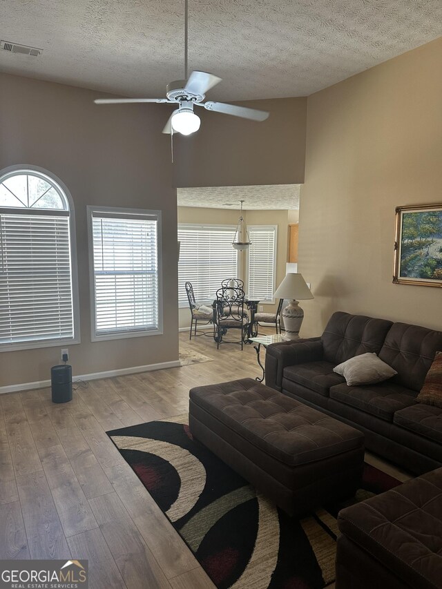 living area featuring light wood-style floors, visible vents, a textured ceiling, and baseboards