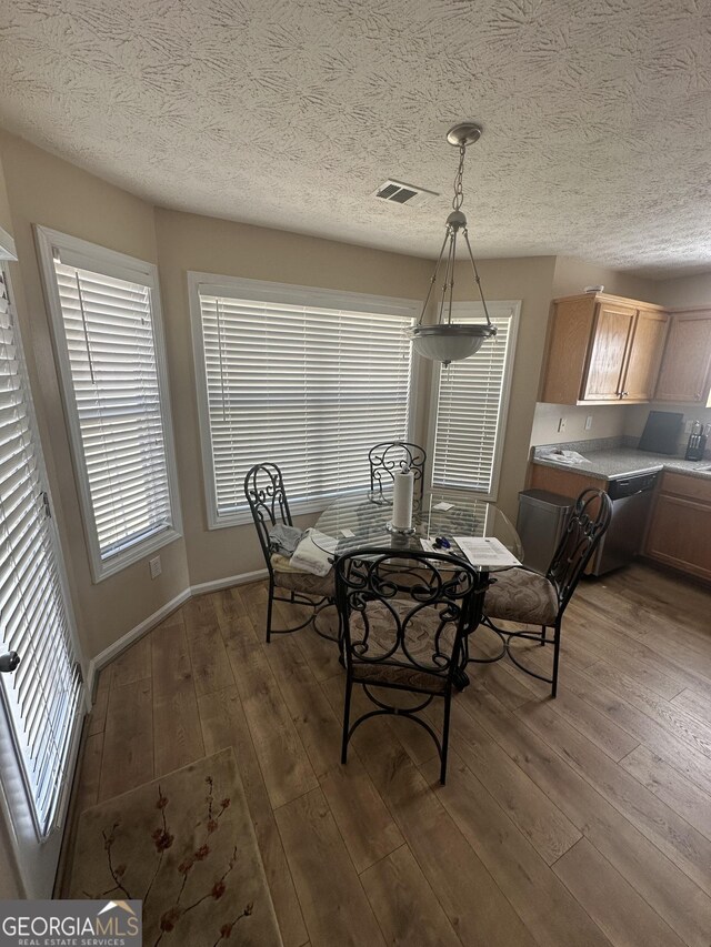 dining area featuring a textured ceiling, hardwood / wood-style flooring, visible vents, and baseboards