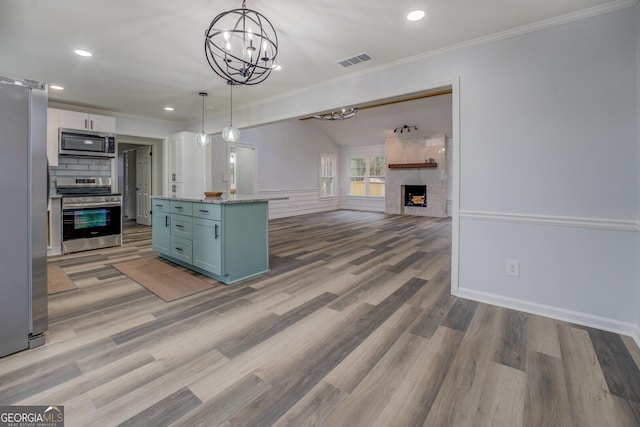 kitchen with visible vents, appliances with stainless steel finishes, light wood-style floors, a large fireplace, and ornamental molding