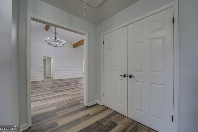 hall with a wainscoted wall, vaulted ceiling with beams, a decorative wall, attic access, and wood finished floors