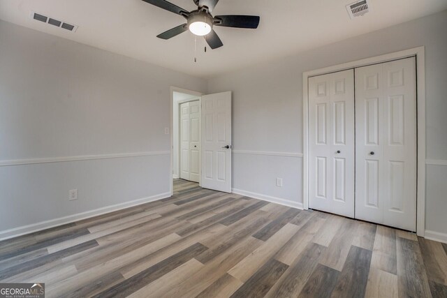 unfurnished bedroom featuring baseboards, a closet, visible vents, and wood finished floors