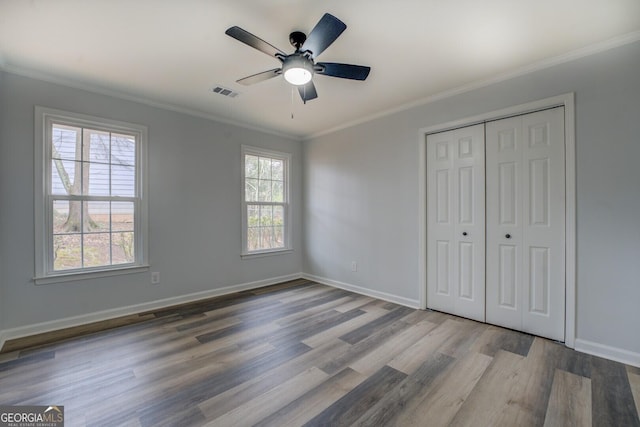 unfurnished bedroom featuring ornamental molding, multiple windows, wood finished floors, and visible vents