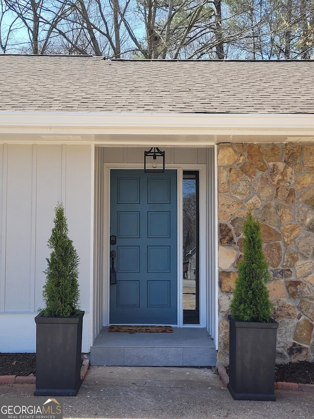 entrance to property featuring a shingled roof and stone siding