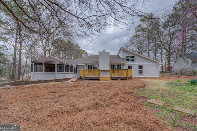 back of house featuring roof with shingles, a chimney, a wooden deck, and a sunroom