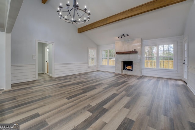 unfurnished living room featuring a chandelier, beamed ceiling, a fireplace, and wood finished floors