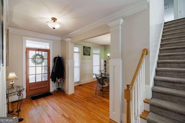 entrance foyer with crown molding, light wood-type flooring, decorative columns, and stairs