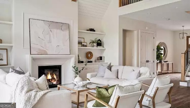 living room featuring built in features, a warm lit fireplace, a high ceiling, and wood finished floors