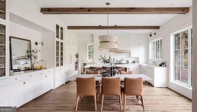 dining area with light wood-style floors, a wealth of natural light, and beam ceiling